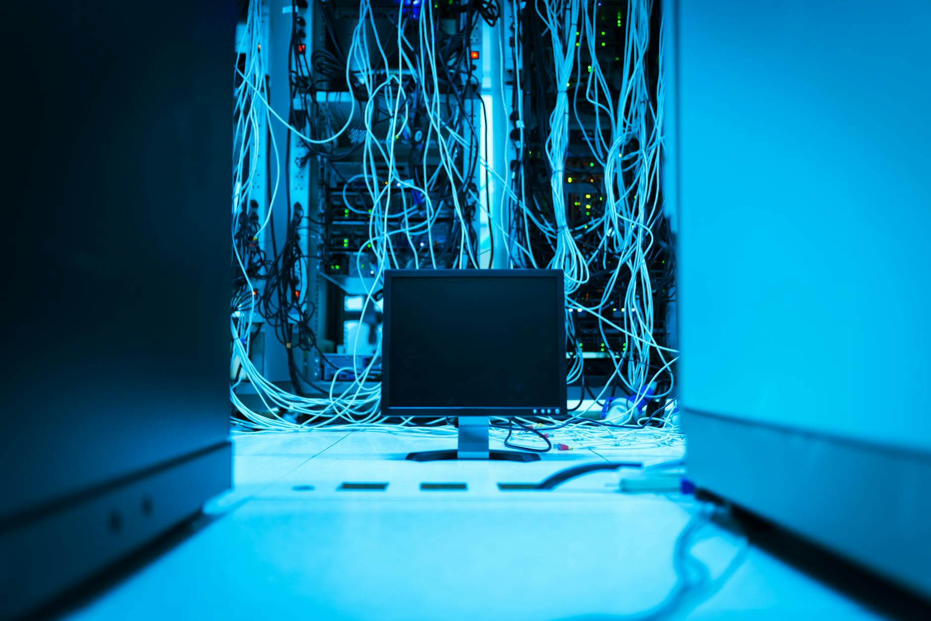 A complex network of cables in a data center with a monitor in the foreground.